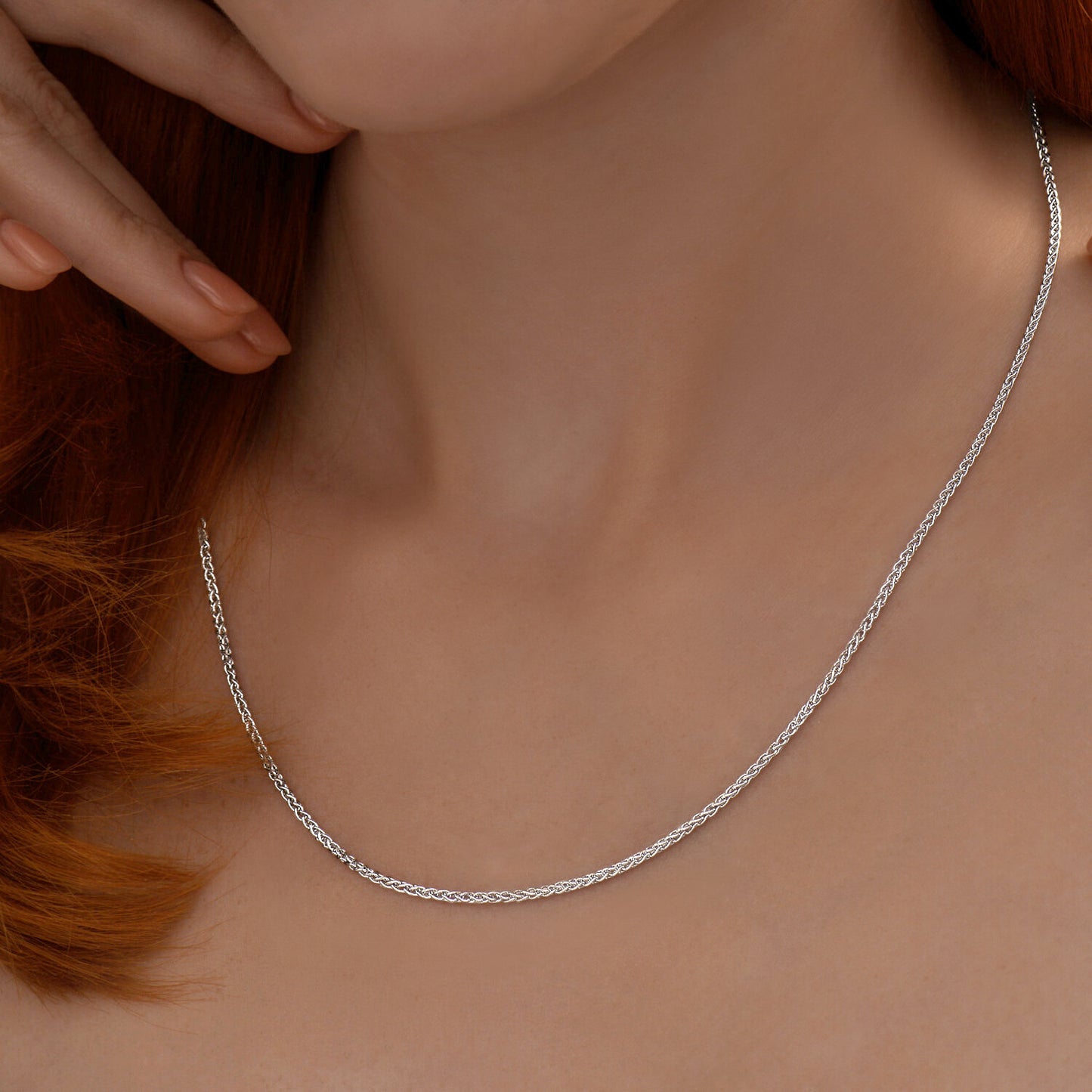 Silver necklace being worn on a person's neck with a neutral background