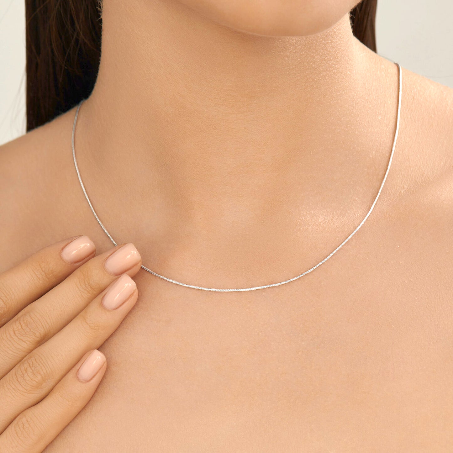 Silver necklace being worn on a person's neck with a hand touching the chest.