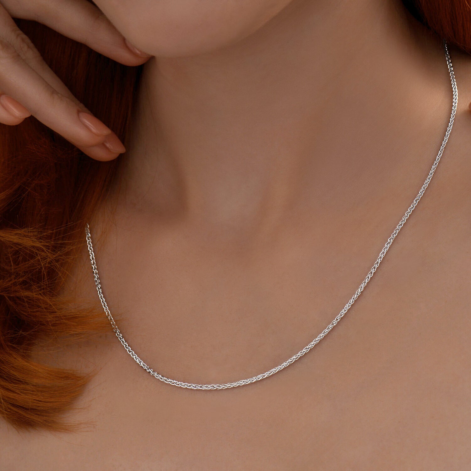 Silver necklace being worn on a person's neck with a neutral background